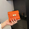 A hand holds an orange leather multi-slot card holder against a dark background.