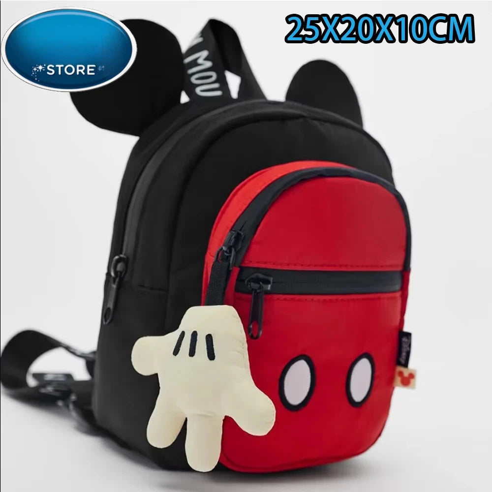 Una mochila negra con un bolsillo delantero rojo y un juguete de peluche blanco.