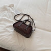 A brown leather mini crossbody bag with a crocodile texture rests on white fabric.
