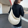 A person wearing a black shirt and light blue jeans is carrying a cream-colored corduroy casual crossbody shoulder bag.