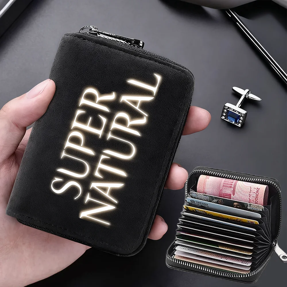 A black compact card wallet with glowing text on the cover is held in a hand next to a stack of credit cards.
