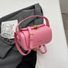 Pinkes Retro-Leder-Schultertasche mit goldener Schnalle neben einem grauen Blazer.