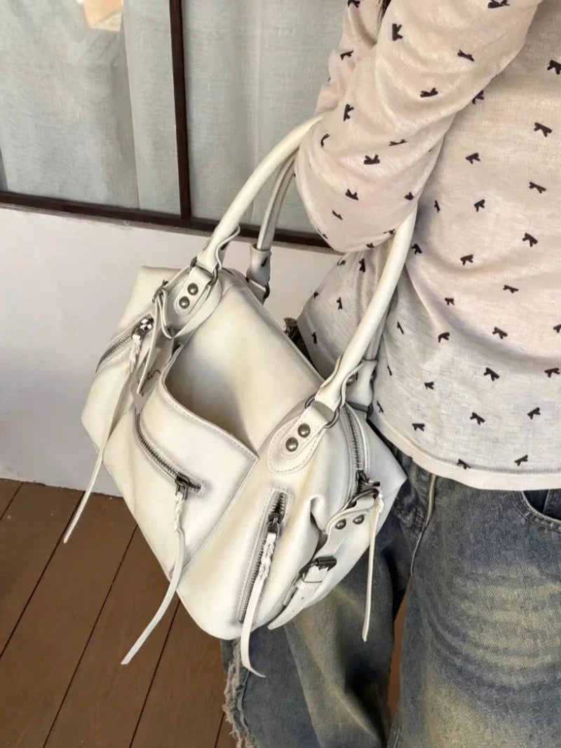 A white vintage PU leather crossbody tote bag with a silver zipper and adjustable strap being held by a person.