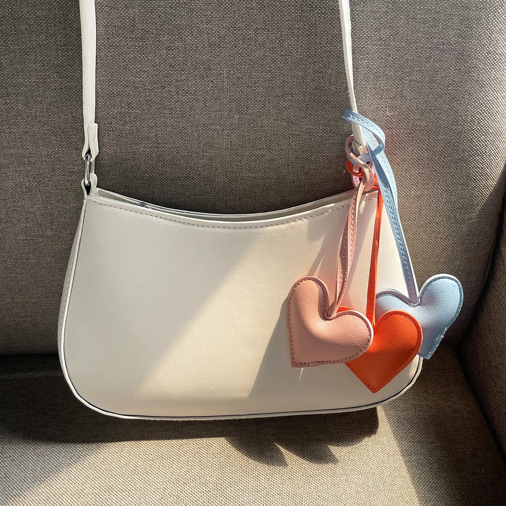 A white PU leather handbag with a strap and three heart-shaped keychains in pink, orange, and blue.