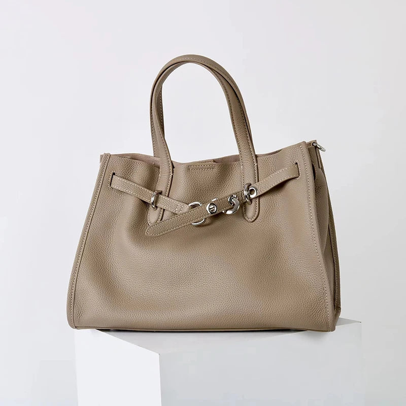 A beige genuine leather women's shoulder tote bag with a top handle resting on a white surface.