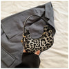 A hand holds a leopard print PU leather mini tote handbag against a gray blazer on a white background.