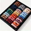 A collection of 19 thin scrunchies hair ties in various shades of satin and silk colors arranged in a black box.