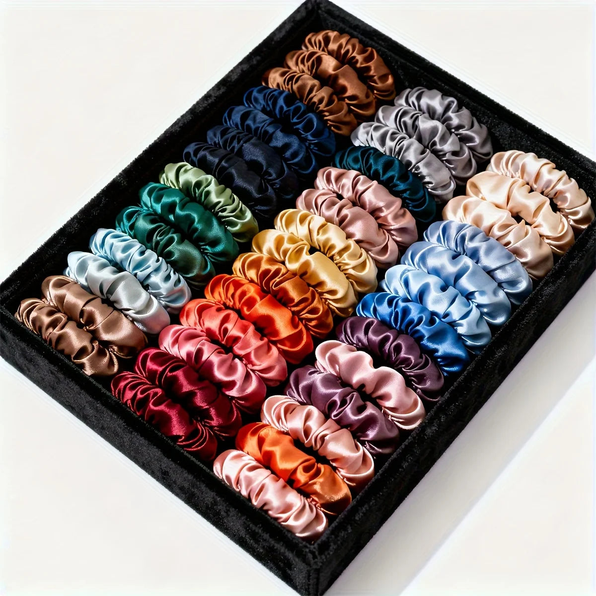A collection of 19 thin scrunchies hair ties in various shades of satin and silk colors arranged in a black box.