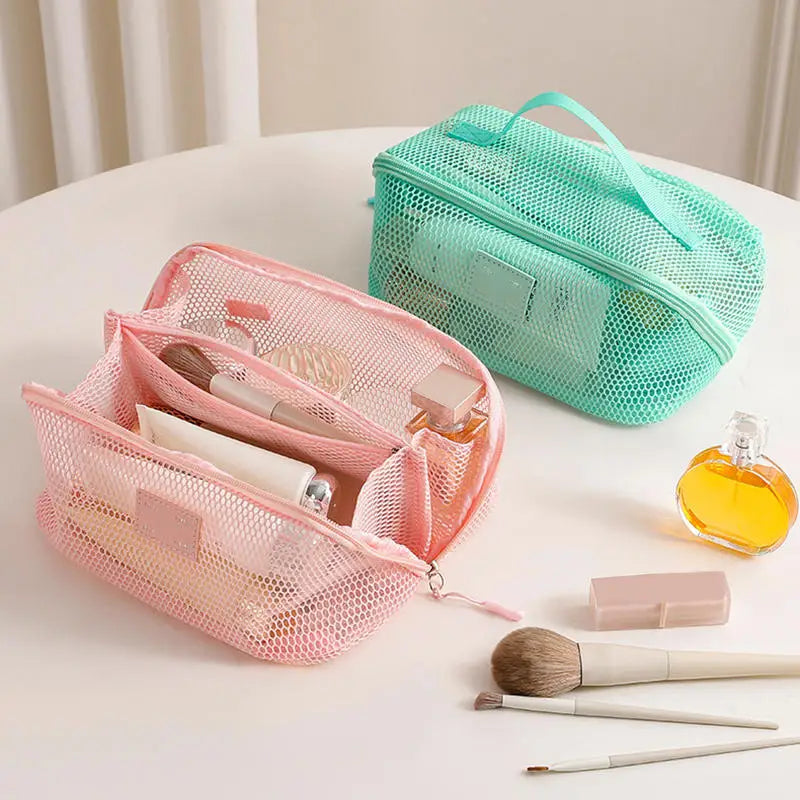 A pink mesh cosmetic organizer pouch next to a teal green mesh pouch and various makeup brushes.