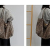 A person is holding a leopard print canvas crossbody tote bag against a light gray shirt.