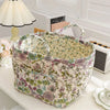 A quilted fabric storage basket with carry handles featuring a floral pattern sits on a white surface.