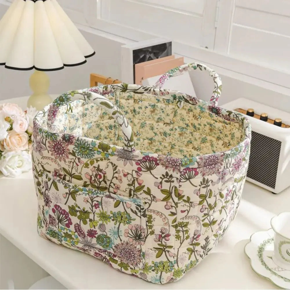 A quilted fabric storage basket with carry handles featuring a floral pattern sits on a white surface.