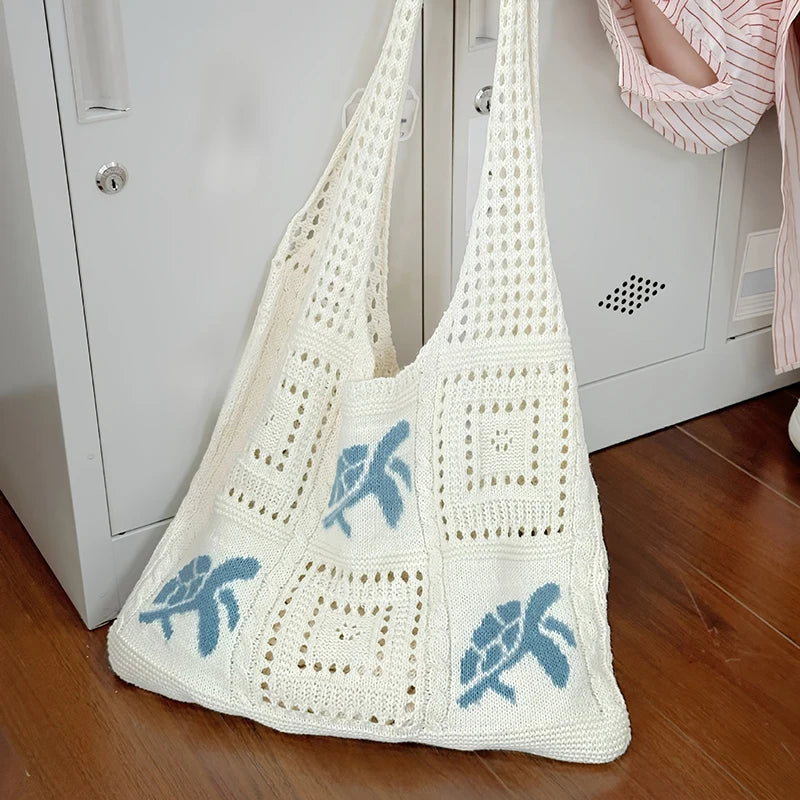 A white knitted tote bag with blue elephant embroidery hanging on a white cabinet door.
