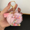 A hand holds a custom initial letter keychain featuring a shiny resin pendant with a pink alphabet charm and pink feathers.