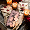 Cartera de cuero sintético rosa para vaca con cierre de cremallera sobre una superficie de madera rodeada de velas y tela.