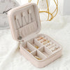 A light pink compact leather jewelry travel box open to display various silver and gold necklaces and rings.