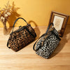 A leopard print faux leather handbag with a top handle and crossbody strap resting on a wooden surface.