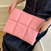 A pink quilted laptop sleeve is being held by a person wearing a dark denim shirt and jeans.