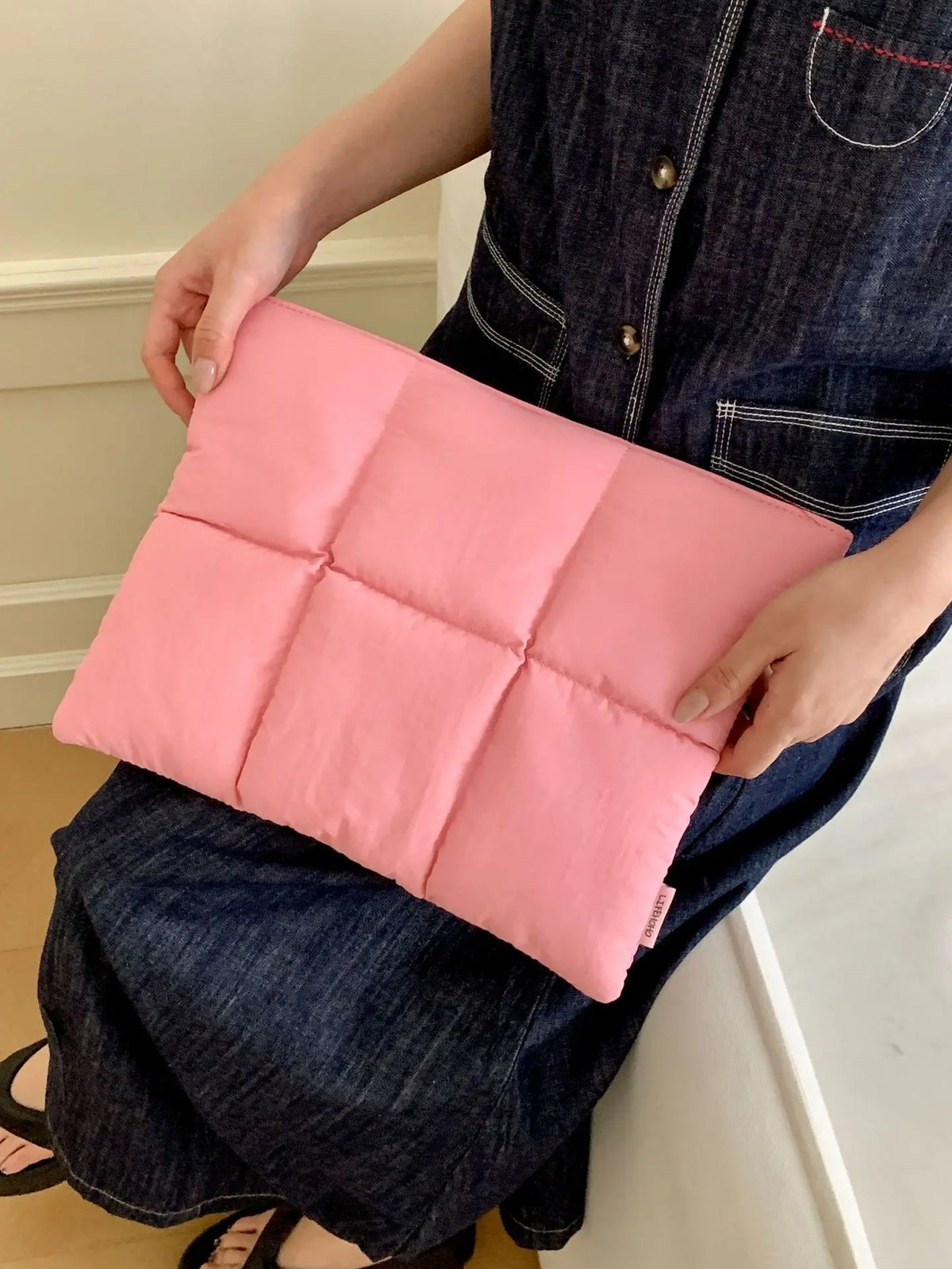 A pink quilted laptop sleeve is being held by a person wearing a dark denim shirt and jeans.