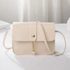 A beige fashion square crossbody bag with a gold chain charm resting on a white surface.
