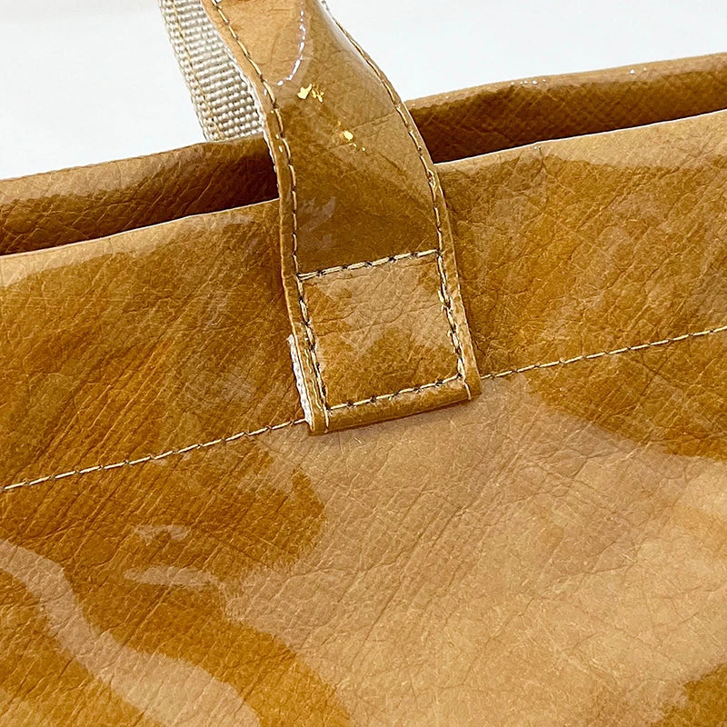 Primer plano de un bolso tote minimalista de PVC marrón mostrando costuras y textura de cuero.