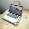 A silver laptop with a screen displaying a mountain landscape is shown inside a light pink protective case on a wooden table.