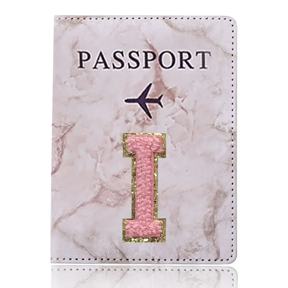 Funda de pasaporte de cuero marmolado rosa claro con la palabra PASAPORTE y una gran inicial I dorada