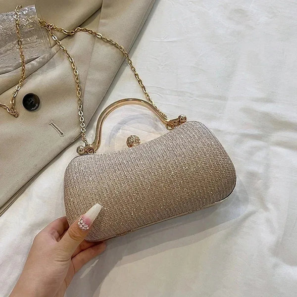 A hand holds a gold chain glitter clutch bag with a round gold charm against a white background.
