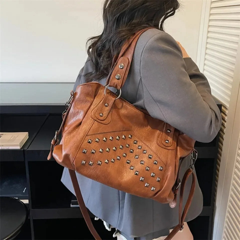A woman is shown from the back carrying a brown leather tote bag with silver rivets and straps.