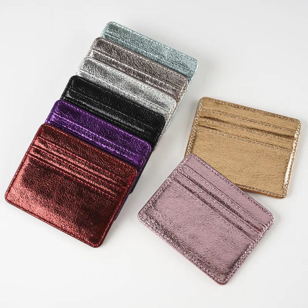 A stack of slim leather mini wallet card holders in various shades including black, purple, and gold.