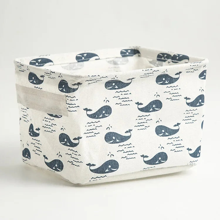 A white storage basket with a blue whale pattern, made of foldable cotton linen, shown from above.