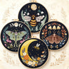 A collection of nine circular embroidery kits featuring detailed butterfly and moon designs on dark fabric.