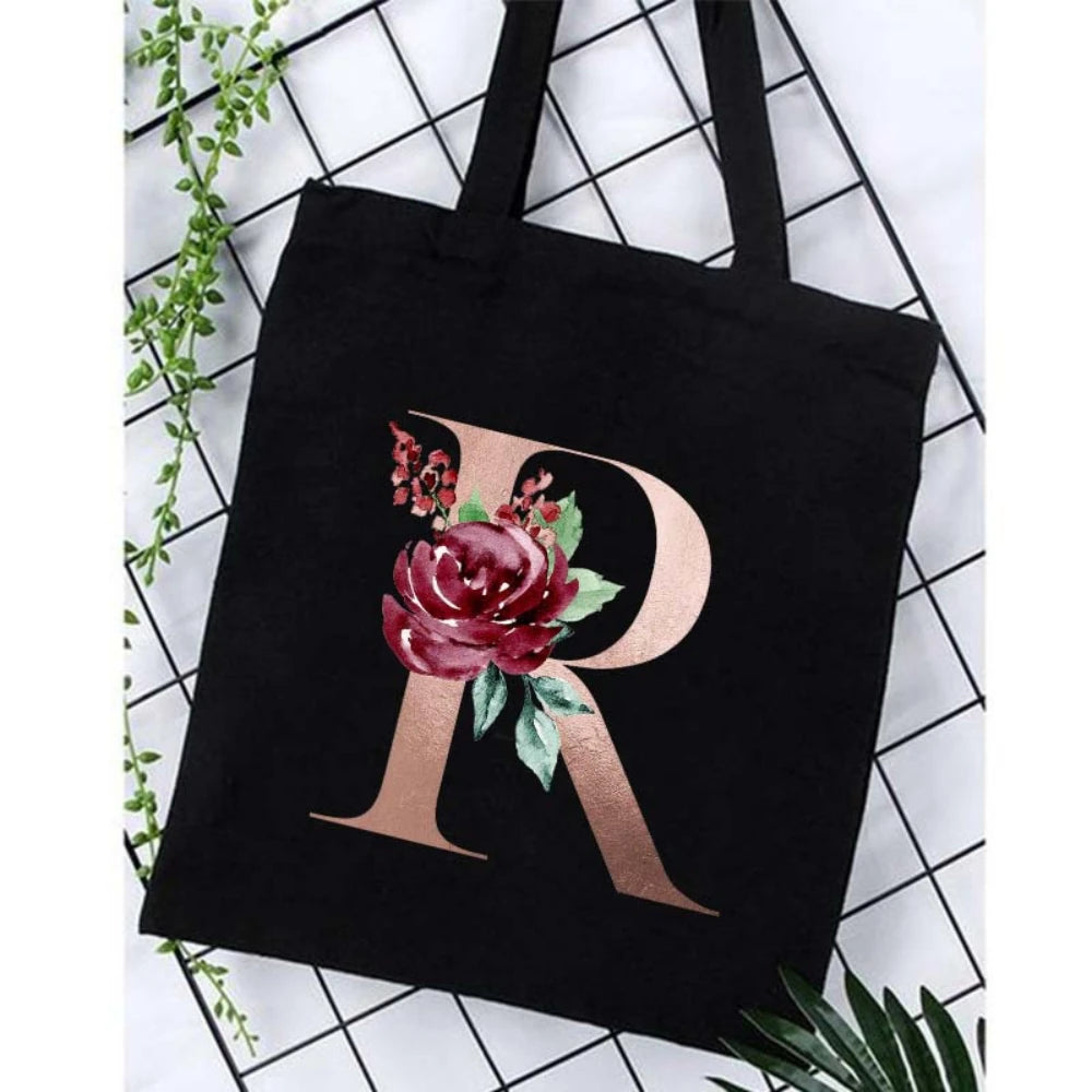 Black canvas tote bag featuring a large gold letter R with floral accents