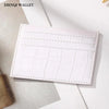 A white leather card holder wallet with a crocodile pattern texture is displayed on a light surface.