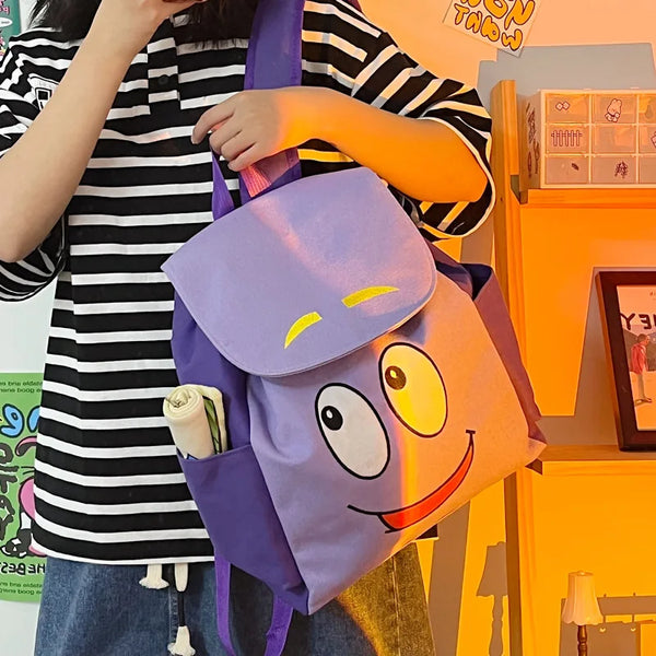 A person is holding a purple Dora The Explorer cartoon flannel backpack against an orange background.