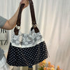 A woman holds a black and white patchwork shoulder bag with a floral pattern against a white background.