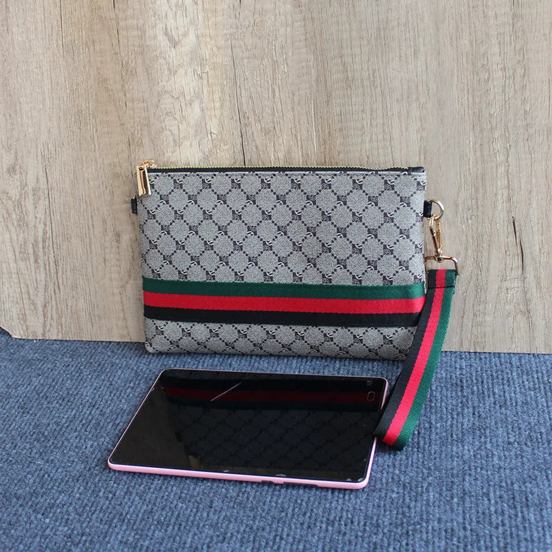 Grau-schwarze Tasche mit grünem Riemen auf blauem Untergrund.