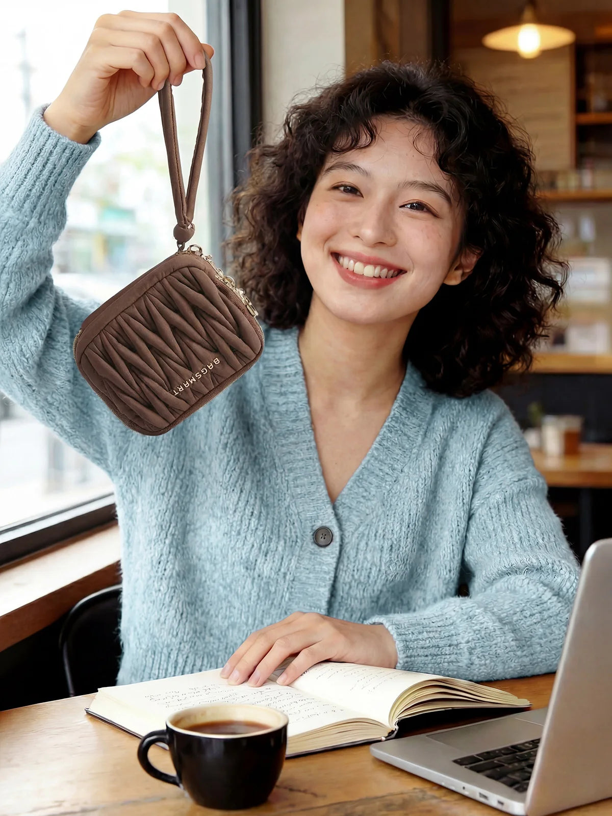 A young woman smiling while holding a brown mini coin purse and card holder wallet next to an open notebook.