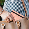 A hand is placing an RFID blocking leather travel wallet into a tan leather handbag.