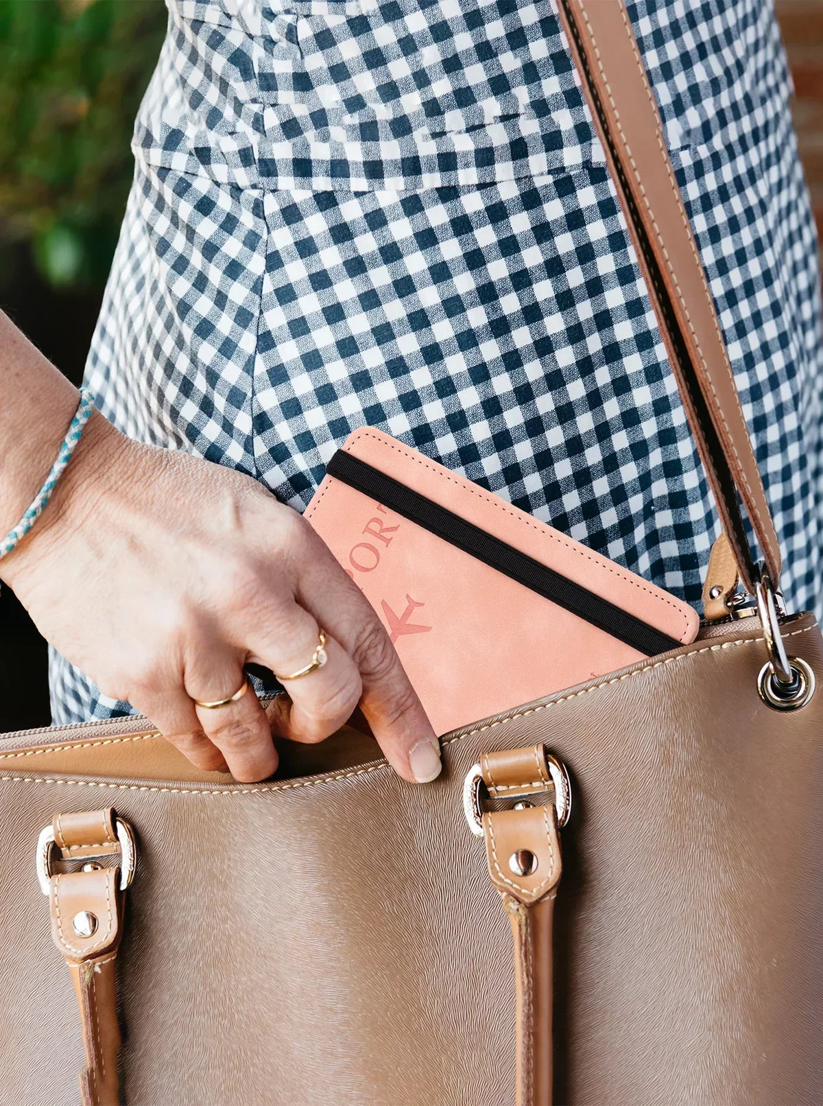 A hand is placing an RFID blocking leather travel wallet into a tan leather handbag.