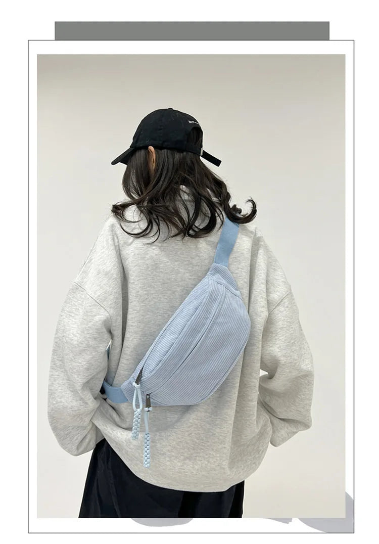 A woman wearing a light gray sweatshirt holds a light blue corduroy waist pack against her back.