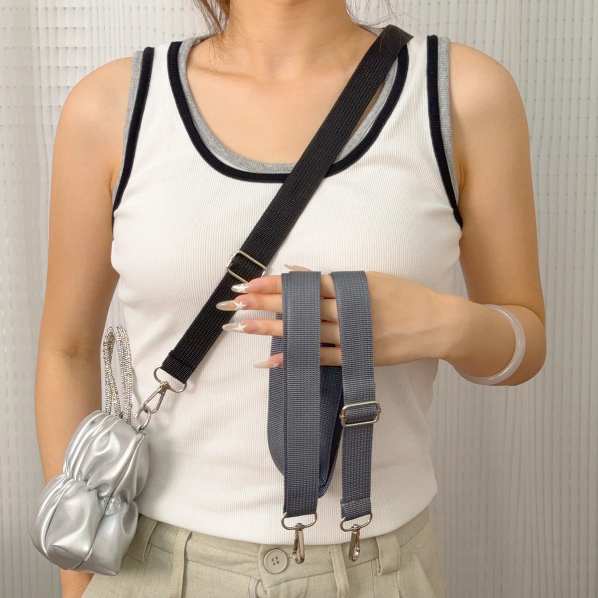 A woman wearing a white tank top holds an adjustable wide shoulder strap for bags and cameras.