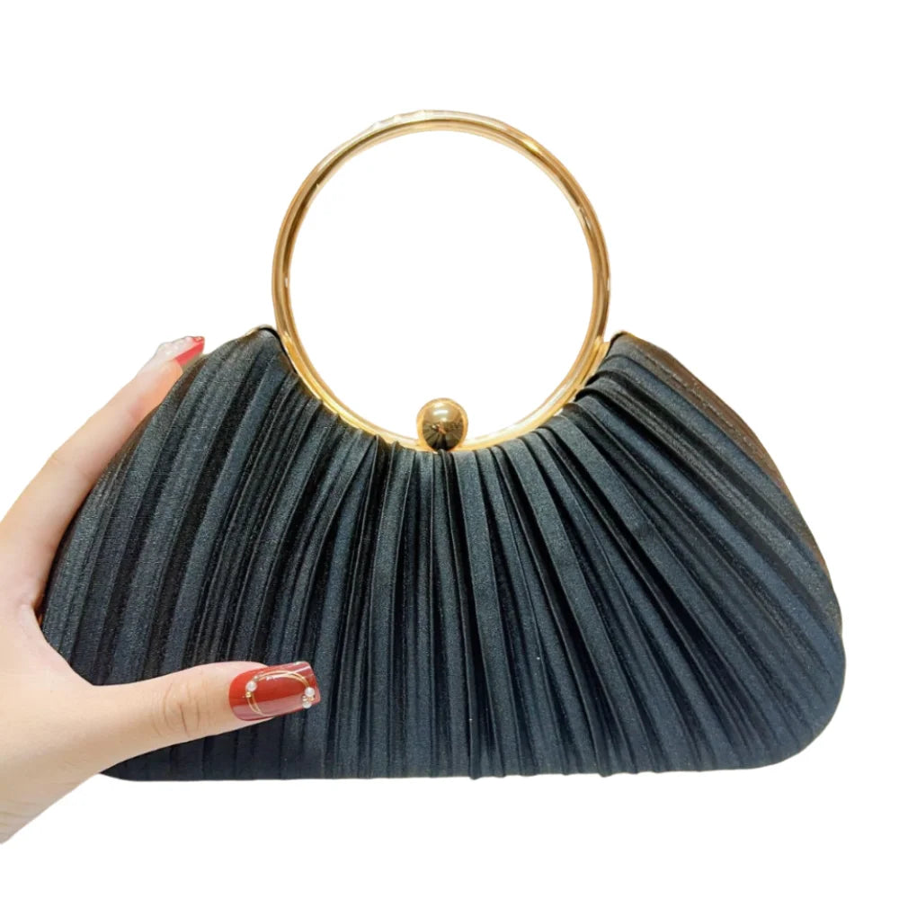A hand holds an elegant black satin pleated evening clutch bag with a gold rim.