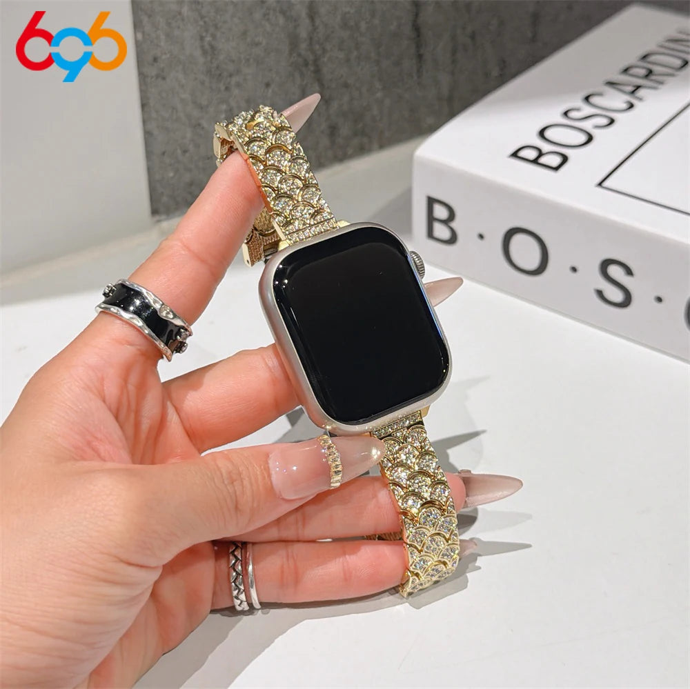 A hand is holding a black Apple Watch with a sparkling gold crystal fishscale metal strap.