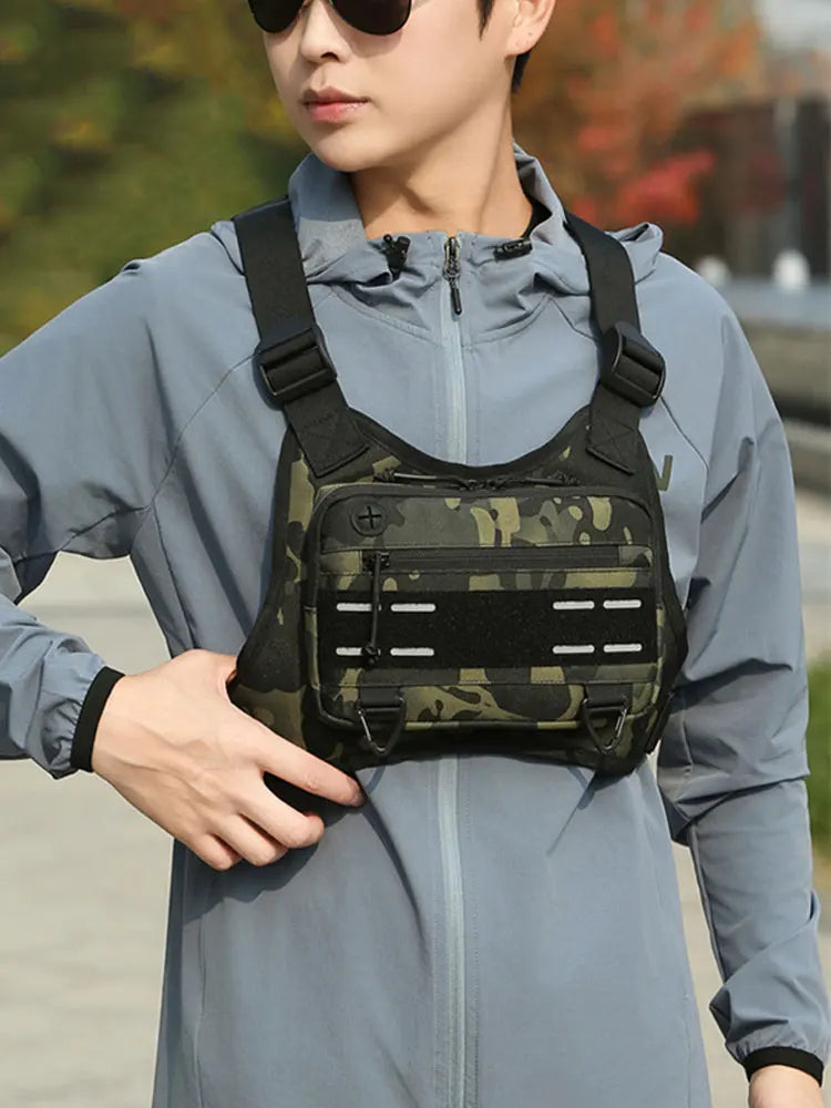 A young man wearing a light blue jacket is holding a black tactical chest rig vest bag for outdoor gear.