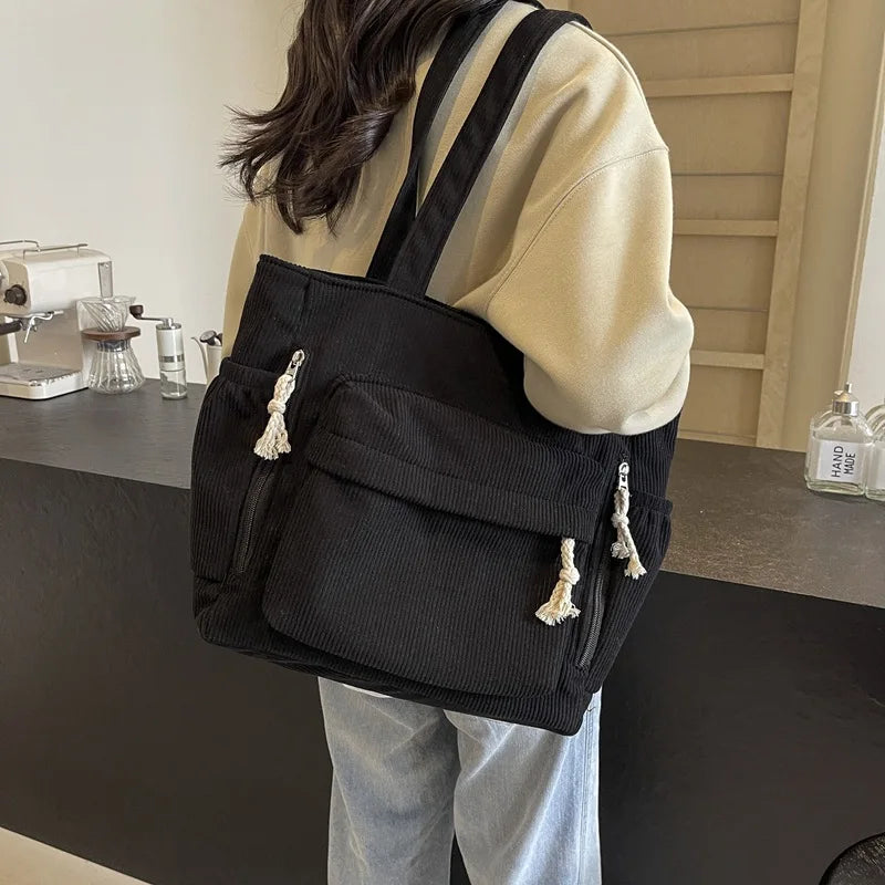 A woman is holding a black corduroy shoulder bag with a zipper on her shoulder.