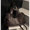A dark brown punk rivet leather tote bag is displayed in a box next to a stack of books.