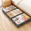 A set of foldable under-bed storage boxes filled with various soft toys and fabric items on a light wooden floor.