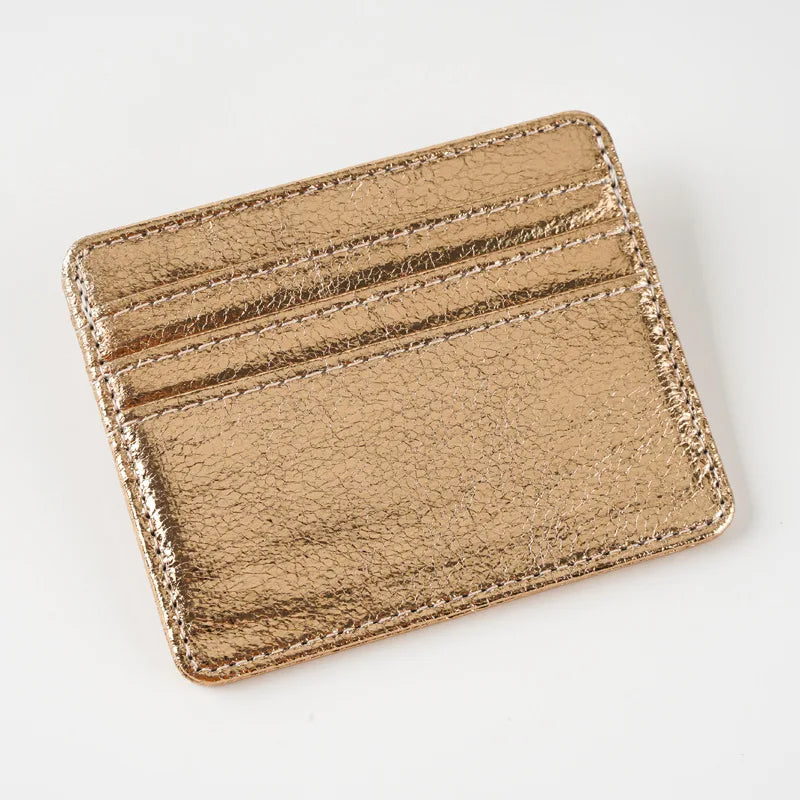A gold-colored slim leather mini wallet card holder with stitched edges.