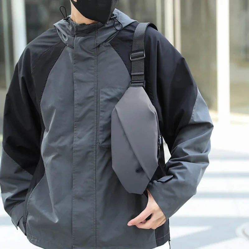 Ein Mann trägt eine schwarze Jacke und hält eine graue minimalistische Lauf-Tauschtasche.